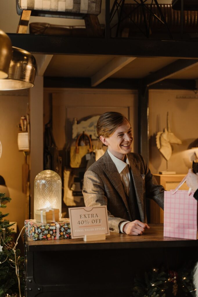 A friendly shop attendant provides a bag to a customer during a holiday sale.